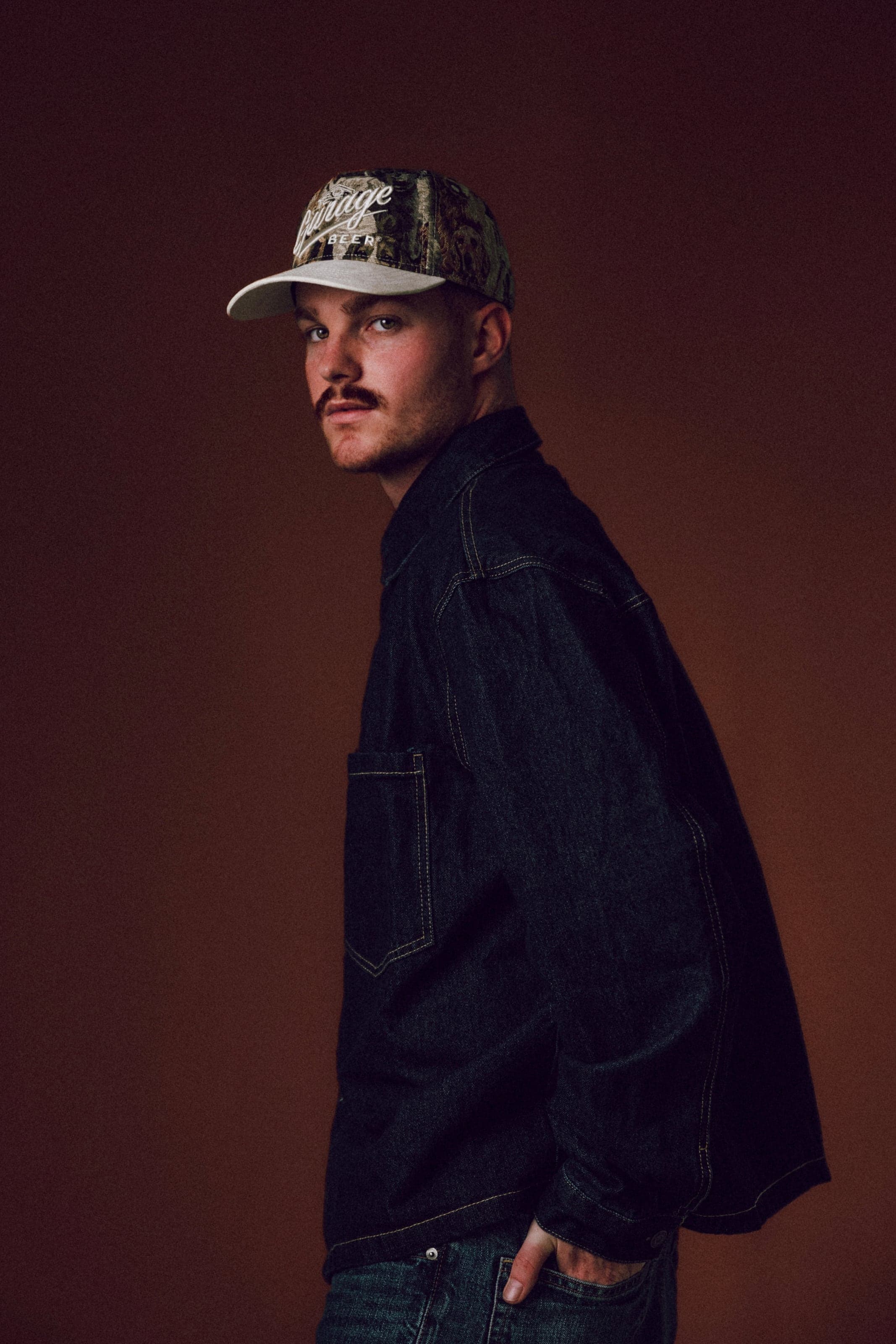 Man in a camo cap and denim jacket on brown
