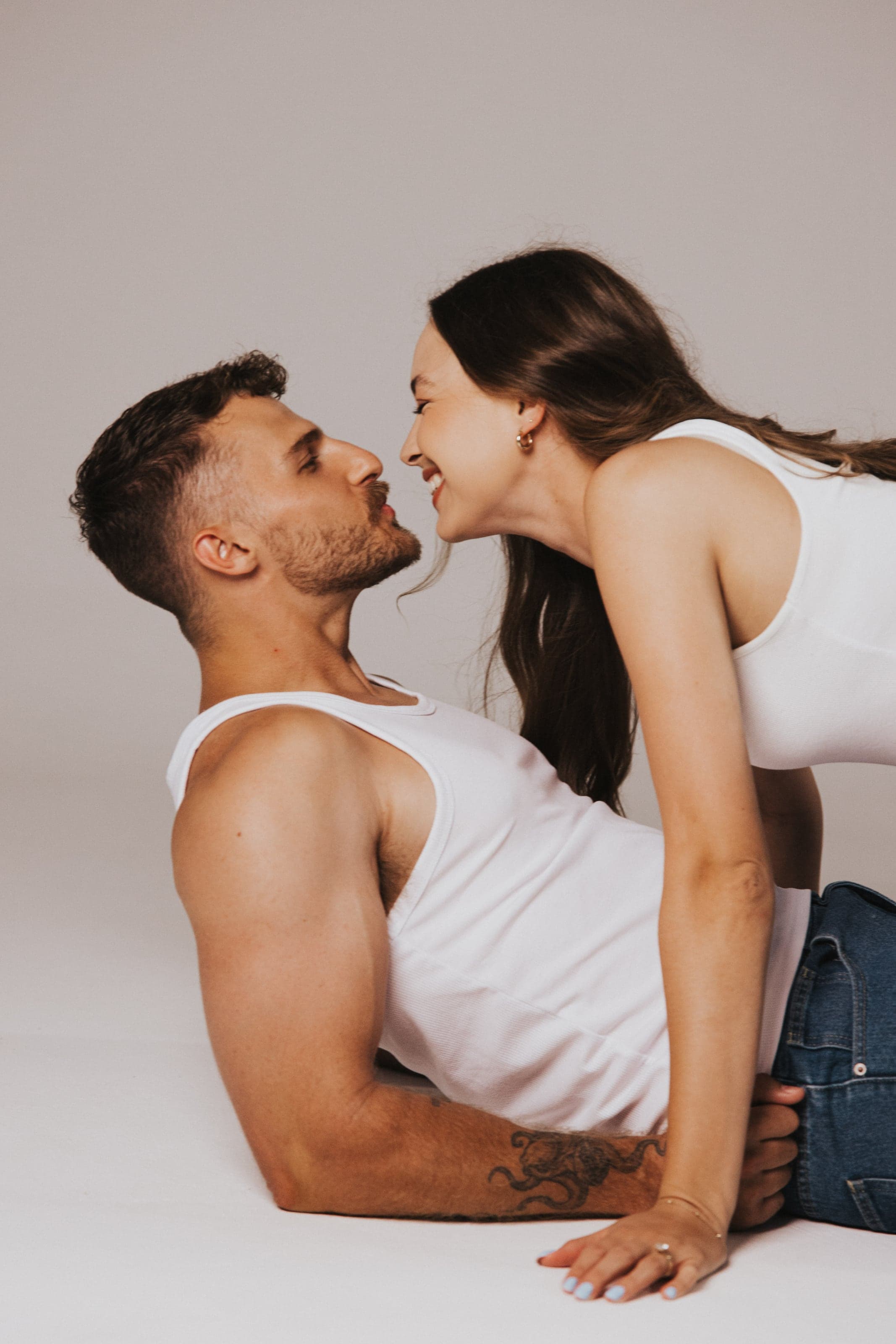 Couple about to kiss, lying on a pale studio floor